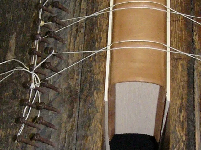 Kézi könyvkötő a könyv gerincén domború fűzési sávokat alakít ki